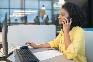 A young woman working in a modern call center environment, engaging in conversation via headset.
